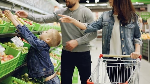 Happy Young Family Mother, Father and Child Are Buying Fruit in Supermarket Putting Pineapple in