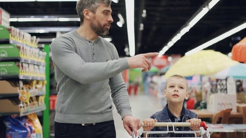 Cheerful Man Is Shopping with His Joyful Child, They Are Walking with Shopping Trolley in