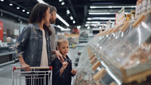 Happy Family Mom, Dad and Cute Kid Are Choosing Food in Large Supermarket, Pointing at Plastic