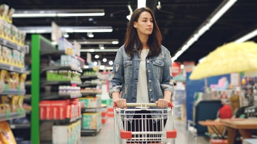 Woman Pushing Shopping Cart Through Supermarket Aisles