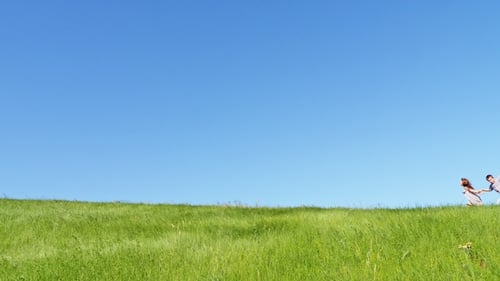 Children Run Along the Top of the Green Hill with a Flying Kite