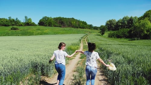 Two Women Holding Hands Running in Crop Field