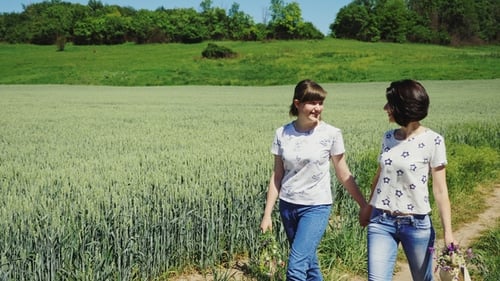 Two Women Walking Hand-in-Hand Through Field