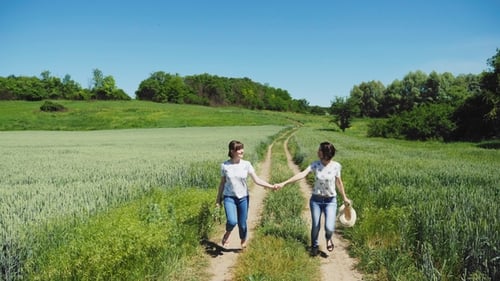 Women Running Hand-in-Hand Through Sunny Rural Fields