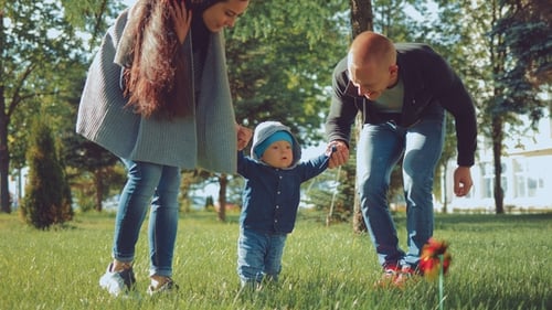 Young Parents Holding Her Young Child As He Practices His First Steps in the Park
