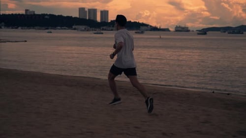 Silhouette of Asian athlete running exercise outside on the beach during beautiful golden sky.
