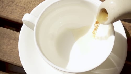 Pouring Fresh Tea into Cup on Wooden Table