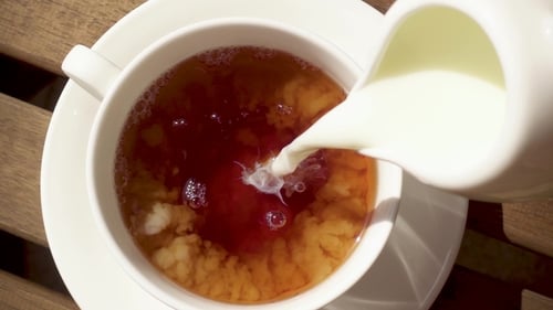 Milk Pouring Into Teacup on Wooden Table