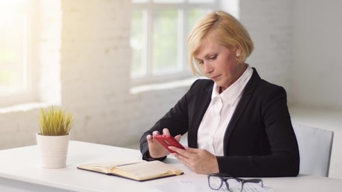 Woman at Desk Looks at Cell Phone and Smiles