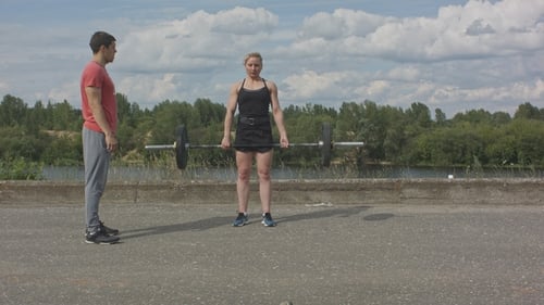 Woman Deadlifting Weights With Man Trainer Outdoors