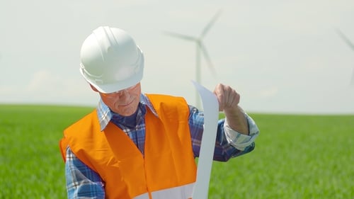 Engineer Analyzing Plan While Looking At Windmills In Farm