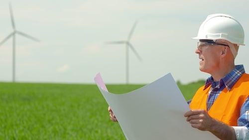 Engineer Analyzing Plan While Looking At Windmills In Farm