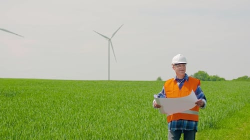 Engineer Analyzing Plan While Looking At Windmills In Farm