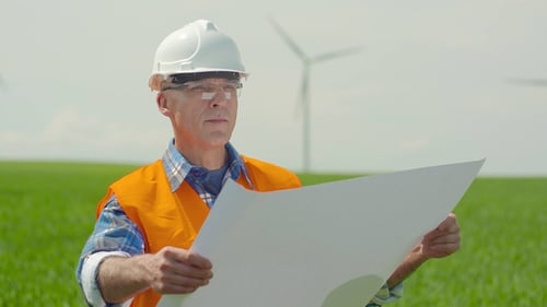 Engineer Analyzing Plan While Looking At Windmills In Farm