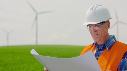Engineer Analyzing Plan While Looking At Windmills In Farm