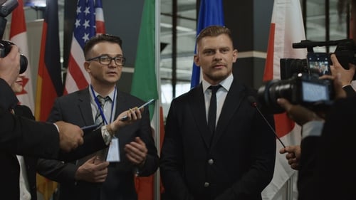 Politician Addresses Press Conference with Flags Background