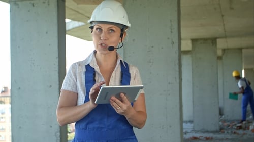 Female Construction Engineer Reading Plans Using Digital Tablet and Talk To Workers