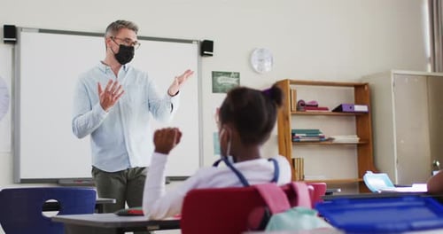Caucasian male teacher wearing face mask teaching students in the class at school