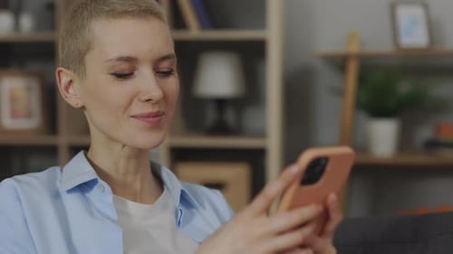 Woman Uses Phone and Smiles While Sitting on Couch