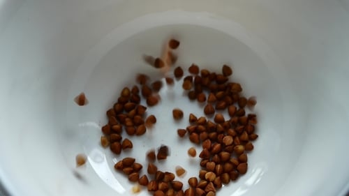 Buckwheat Grains Being Poured into a White Bowl