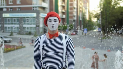 Lustiger Pantomime in roter Baskenmütze zeigt Daumen hoch am Springbrunnen-Hintergrund