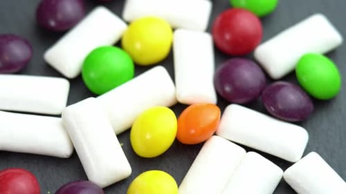 Sweets Colored Candies Skittles and Mint Chewing Pads Colored Sweets Rotate on a Black Plate