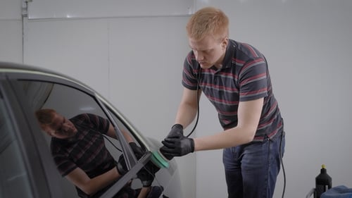 Professional Worker of Carwash Station Carefully Polishing Clean Car with a Polishing Machine.