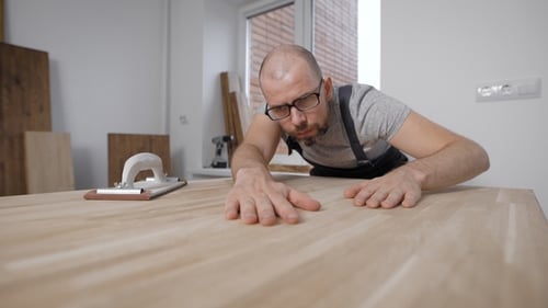 Man Inspecting Smooth Wooden Table Surface