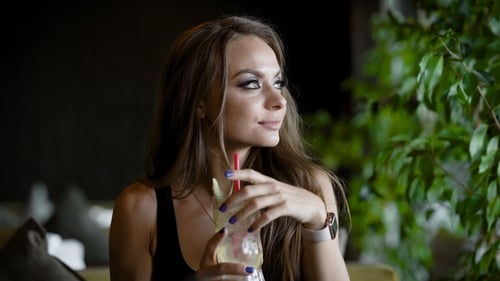 Alone Pretty Woman Is Drinking Cocktail with Ice Through Straw, Sitting in a Cafe in Daytime