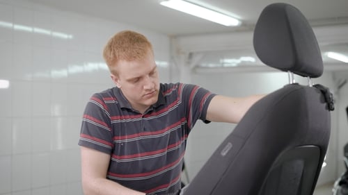 Worker Is Vacuuming Removed Black Car Seat in a Room of Auto-service During Cleaning, Car Washing