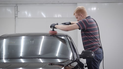 Master Is Grinding a Roof of Clean Black Automobile During Making Protective Covering in a Garage