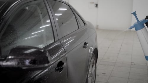 Washerman Is Spraying Water By Nebulizer on a Black Car Body in a Car Wash Box, of Hands