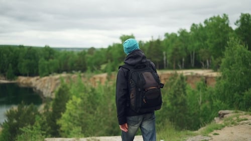 Portrait of Young Man Tourist with Knapsack Walking Down the Hill and Watching Exciting View Under