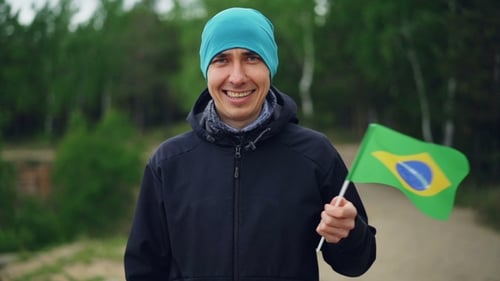 Porträt eines freudigen Reisenden, der brasilianische Flagge schwenkt und mit einem frohen Lächeln in die Kamera blickt