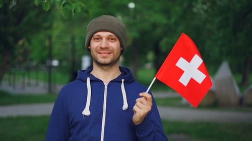 Man Smiling Holding Swiss Flag in Urban Park