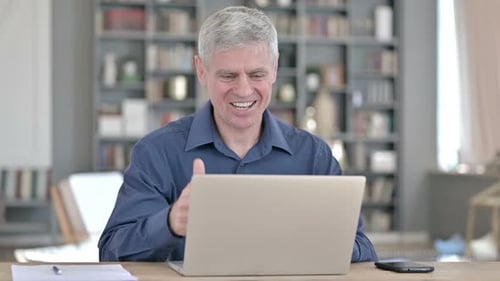 Cheerful Middle Aged Man Doing Video Chat on Laptop in Office