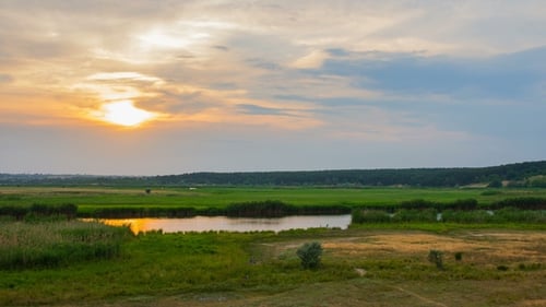 Sunset Over River with Reeds and Forest Under Blue Clouds