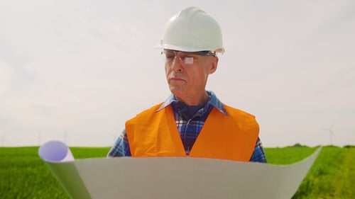 Engineer Analyzing Plan While Looking At Windmill Farm. Eco Energy Concept.