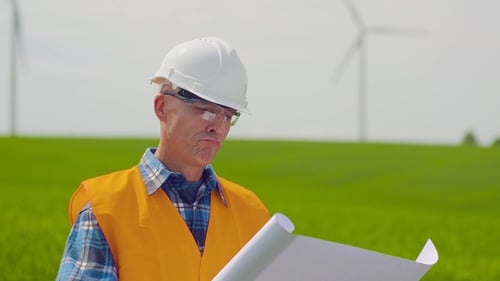 Engineer Analyzing Plan While Looking At Windmill Farm. Eco Energy Concept.