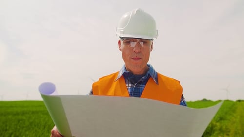 Engineer Analyzing Plan While Looking At Windmill Farm. Eco Energy Concept.