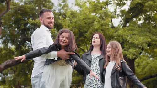 Cheerful Parents and Their Two Little Daughters Relaxing at Green Garden with
