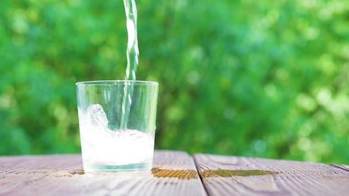 Kohlensäurehaltiges Mineralwasser gießt in ein Glas verschwommene Baumblätter im Hintergrund, Konzept von