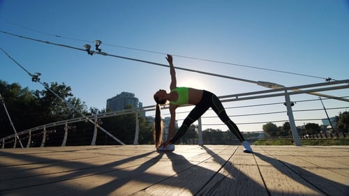 Active Woman Silhouette Exercising and Stretching in City Park on Footbridge