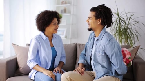 Man Gives Flowers to Woman on Sofa