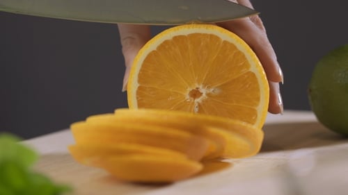 Frau schneidet Orange mit einem Messer auf einem Küchentisch. Frau macht frischen Orangensaft.