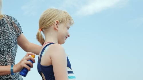 Mama trägt im Urlaub den Sonnenschutz ihrer Tochter vor der Sonne auf