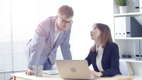 Young Man Pointing at Laptop Discussing Something with Her Coworker While Standing at Office