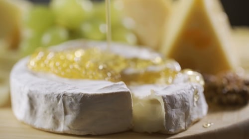 Honey Is Poured Onto a Cheese Plate with Different Cheeses, Grapes and Nuts