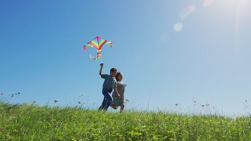 Children Running With Kite in Green Field on Sunny Day