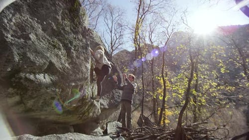 Young woman climbing rock as man spots her from below